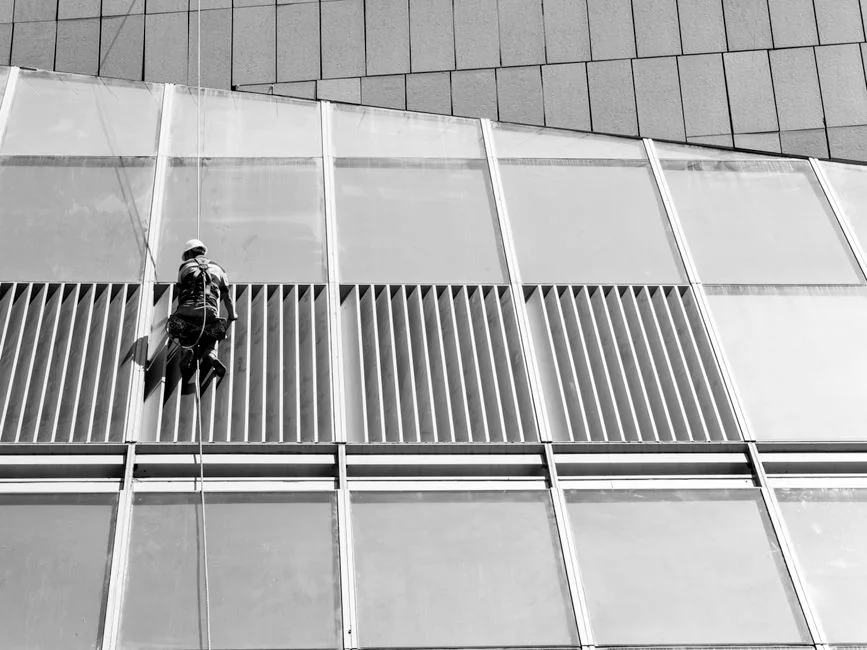 Three window cleaners suspended on ropes clean a modern glass building facade during the day.