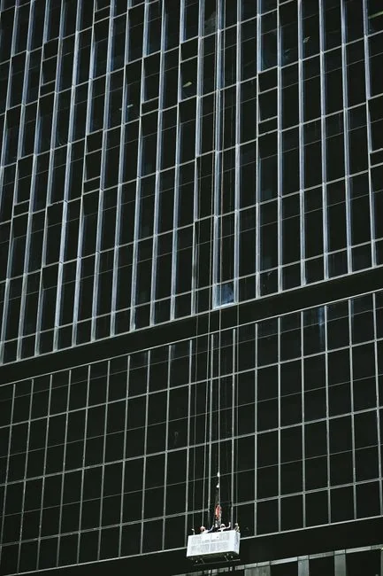 A worker cleaning skyscraper windows with a harness in an urban setting.